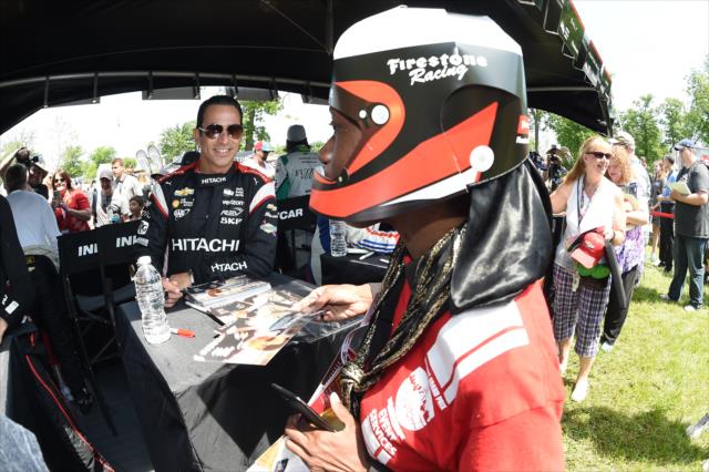 Helio Castroneves looks over a paper helmet of a volunteer during the autograph session at Belle Isle Park in Detroit -- Photo by: Chris Owens