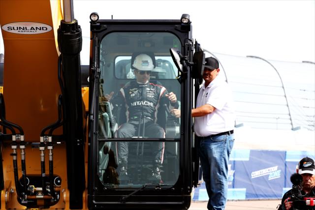 Helio Castroneves receives instructions to operate an excavator to break ground for the Phoenix International Raceway modernization project -- Photo by: Chris Jones