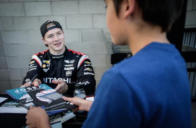 Josef Newgarden signs a book after his likeness for a young fan during the autograph session at ISM Raceway -- Photo by: Shawn Gritzmacher